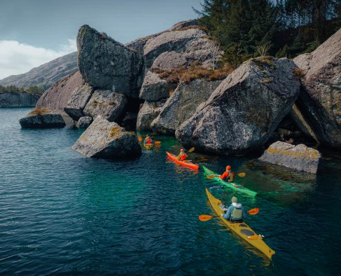 Guided kayaking group paddling through calm waters with mountain views in the distance.