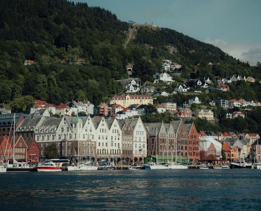 Bryggen Waterfront in Bergen, Norway A scenic view of Bryggen in Bergen, Norway, featuring colorful wooden buildings along the waterfront, boats in the harbor, and hillside homes framed by lush nature.